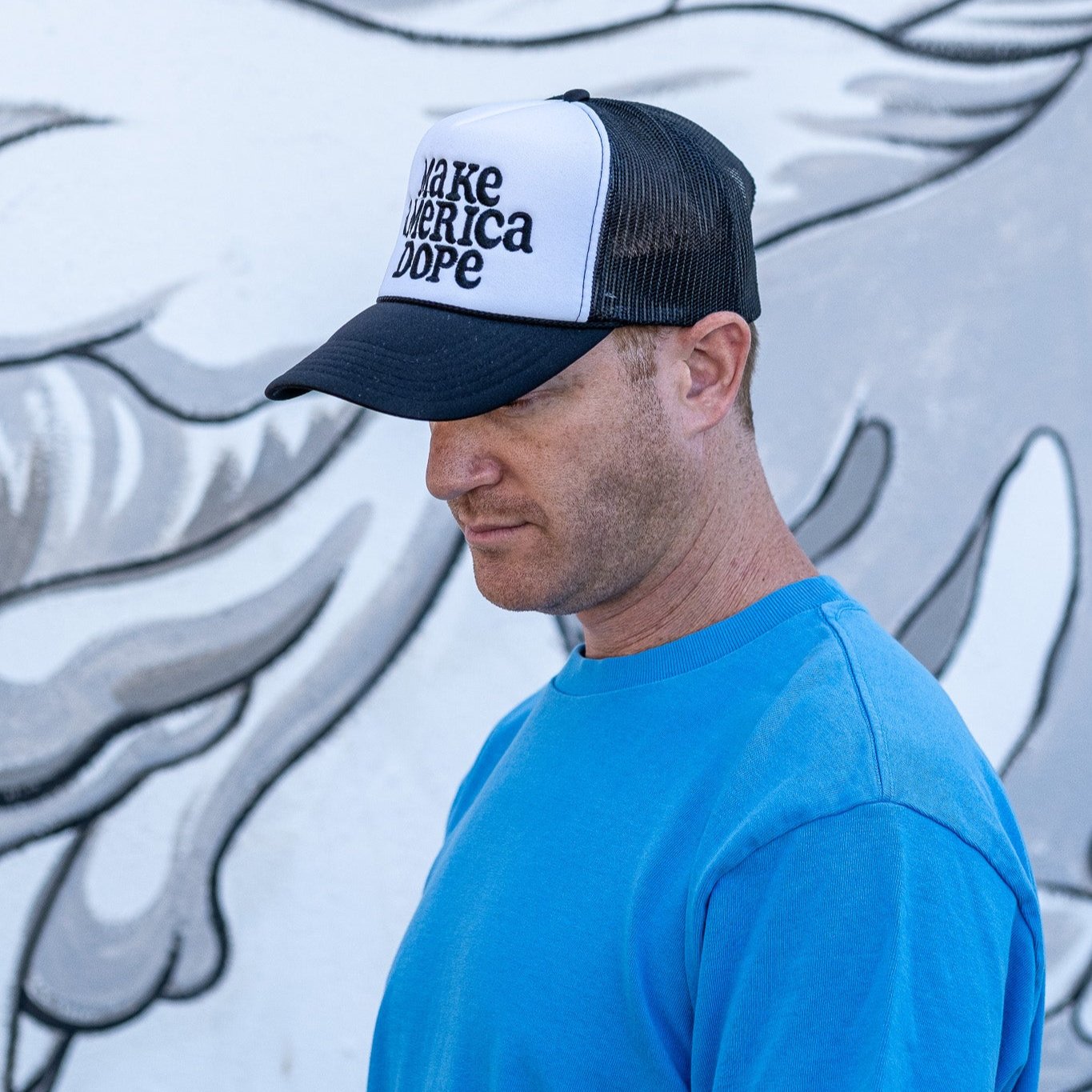 Man standing in front of graffiti wall wearing black and white Make America Dope Hat.