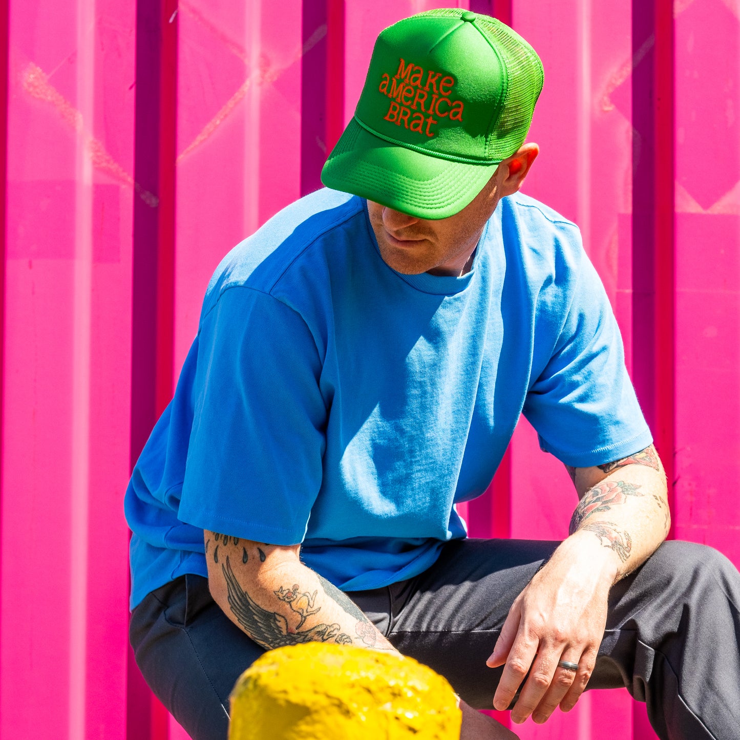 Man sitting in front of pink shipping container wearing green and orange make america brat hat