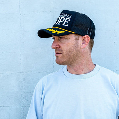 Man standing in front of white wall wearing black white and gold make america dope hat