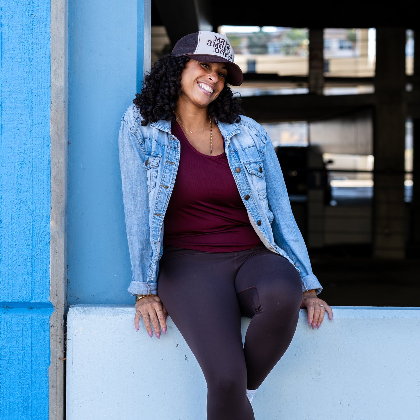 Woman sitting on cement wall wearing brown and tan Make America Dope hat 