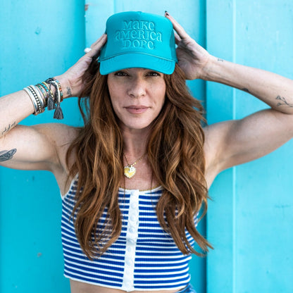 Woman standing in front of teal wall wearing teal make america dope hat