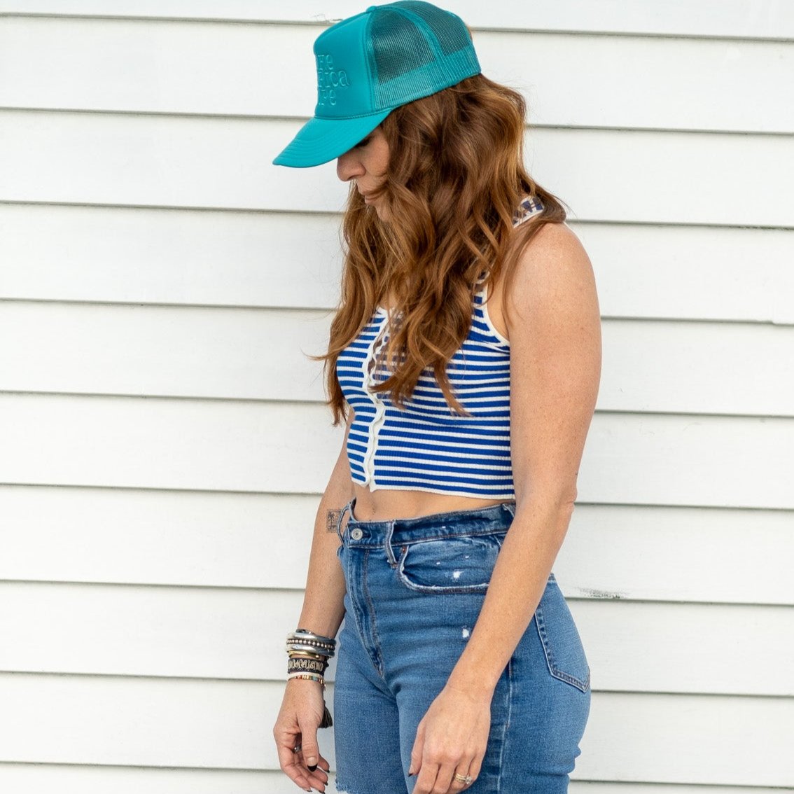 woman standing in front of white wall wearing teal make america dope hat